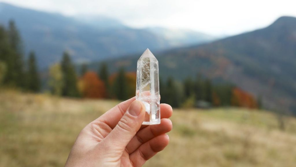 Holding cut clear quartz crystal with mountains background