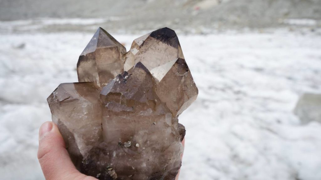 Hand holding large cluster of smoky quartz with snow background