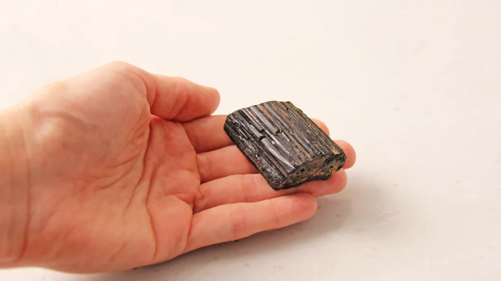 Hand holding rough black tourmaline crystal