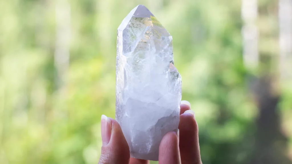 Holding clear quartz stone with green background